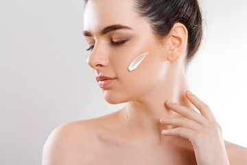 Woman applying skincare cream on her face while showcasing a healthy skin glow in a bright and minimalistic setting, capturing a moment of self-care and beauty