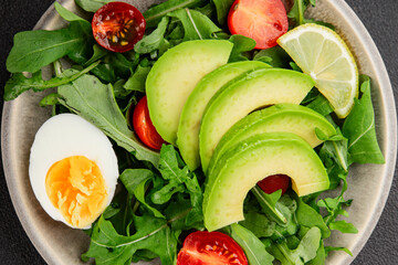 Avocado salad arugula, egg, tomato, mixed greens, vegetables dish fresh delicious gourmet food background tabletop rustic food top view copy space keto and paleo diet vegetarian food