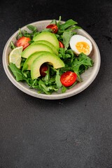 Avocado salad arugula, egg, tomato, mixed greens, vegetables dish fresh delicious gourmet food background tabletop rustic food top view copy space keto and paleo diet vegetarian food