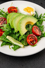 Avocado salad arugula, egg, tomato, mixed greens, vegetables dish fresh delicious gourmet food background tabletop rustic food top view copy space keto and paleo diet vegetarian food