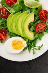 Avocado salad arugula, egg, tomato, mixed greens, vegetables dish fresh delicious gourmet food background tabletop rustic food top view copy space keto and paleo diet vegetarian food
