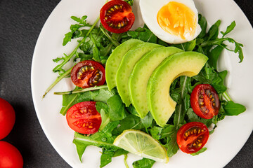 Avocado salad arugula, egg, tomato, mixed greens, vegetables dish fresh delicious gourmet food background tabletop rustic food top view copy space keto and paleo diet vegetarian food