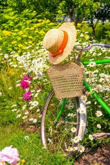 Straw hat, wicker basket on a vintag bicycle in a blooming summer garden