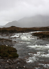 Scottish mountain loch in autumn surrounded by mountain peaks and rugged slopes, with water reflecting the dramatic highland landscape in Scotland