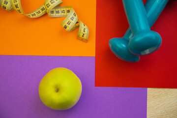 Fresh green apple on colorful surface with measuring tape and dumbbells, representing healthy living, fitness goals, and wellness choices in a vibrant setting