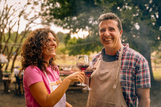Smiling couple enjoying outdoor celebration with wine glasses and aprons