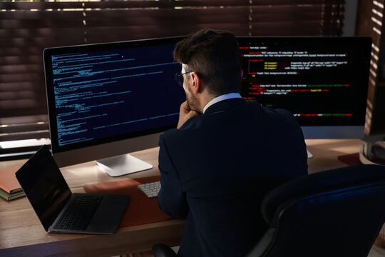 Programmer working on computer with dual monitors and laptop at table in office, back view
