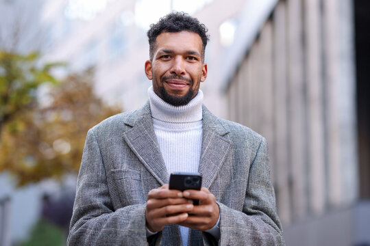 Portrait of handsome man in suit with smartphone on city street, low angle view