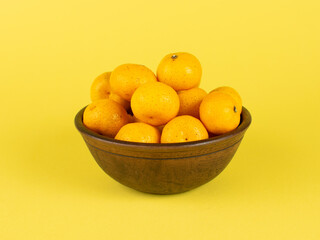 Rustic Wooden Bowl Filled with Ripe Oranges on a Vibrant Yellow Background