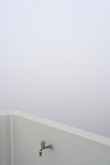 A fragment of a wall against a backdrop of thick fog and smog. A beige wall of an open roof or terrace with a water tap. Concept of air pollution. Minimalistic vertical photo with copy space.