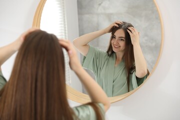 Fototapeta premium Woman using talcum powder as dry shampoo near mirror at home