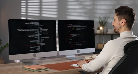 Programmer working on computer with dual monitors at table in office