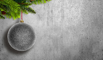 Silver Christmas bauble hanging from green fir branches on a gray concrete background. Minimalist holiday composition with space for text, perfect for winter and festive designs