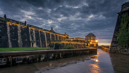 Fototapeta premium Stone fortress with illuminated walls under a cloudy sky.