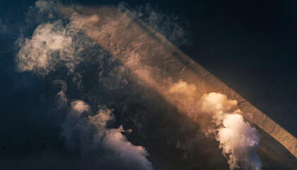 Smoke billows against a textured wall illuminated by a diagonal light beam.