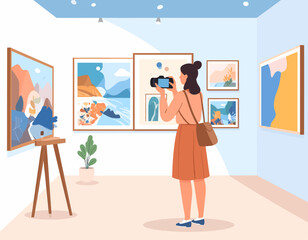 A woman with a shoulder bag takes a photo of artwork in an art gallery filled with paintings and plants.