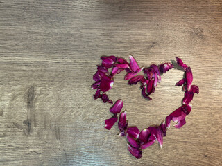 Heart made of pink rose petals on a wooden surface. Romantic, festive background with space for text. Soft lighting.