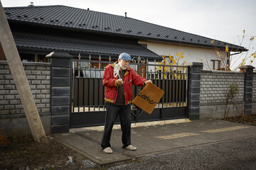 Elderly man holding welcome mat outside modern house on sunny afternoon