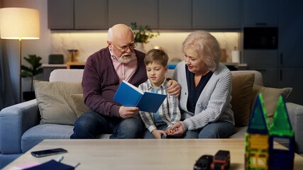 Happy grandparents reading a book to little grandson at home, family pastime - Powered by Adobe