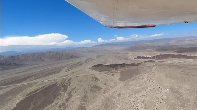 Aerial footage from an aircraft window showing the arid Nazca desert landscape below while flying towards the famous ancient geoglyphs in Peru