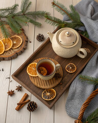 Hygge wooden table setup with tea pot, dried oranges, pine branches, warm natural textures, top-view background
