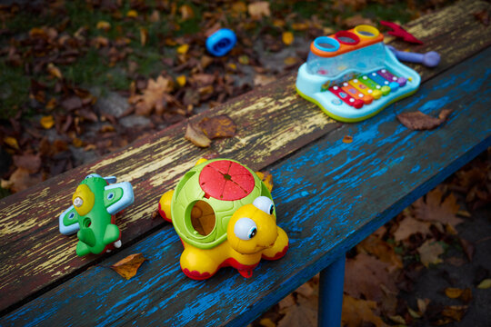 Colorful children's toys on a bench in a park surrounded by autumn leaves during a sunny day - Powered by Adobe
