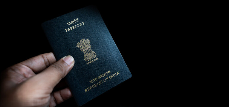 A person holds an Indian passport against a dark background, highlighting the cover’s golden emblem and text