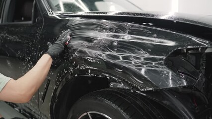 Detailing experts carefully washing a black car's hood, applying soap foam and cleaning the automotive surface by hand