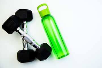 Dumbbells and a green water bottle are arranged on a white surface, symbolizing fitness and hydration, ideal for promoting a healthy lifestyle and exercise routines