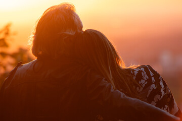 Zwei Menschen sitzen eng beieinander, R&uuml;ckenansicht, warmes Licht, romantische Stimmung, Sonnenuntergang, verschwommene Landschaft im Hintergrund.