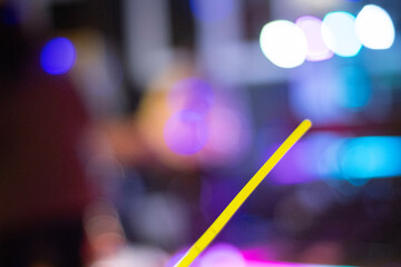 Abstrakte Aufnahme mit bunten, unscharfen Lichtern im Hintergrund, ein gelber Strohhalm im Fokus, Nacht, Party-Atmosph&auml;re.
