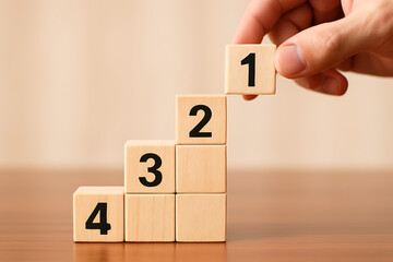 Hand stacking a wooden cube with the number one on top of a step pyramid of blocks numbered two, three, and four symbolizing progress and rising success in a sequence