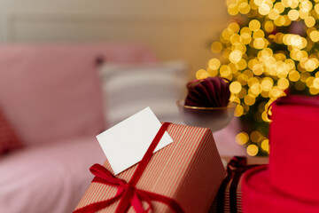 Close-up of a blank card on a wrapped Christmas gift in front of an illuminated Christmas tree