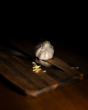 Close-up of a bulb of garlic on a wooden chopping board with a sliced clove of garlic