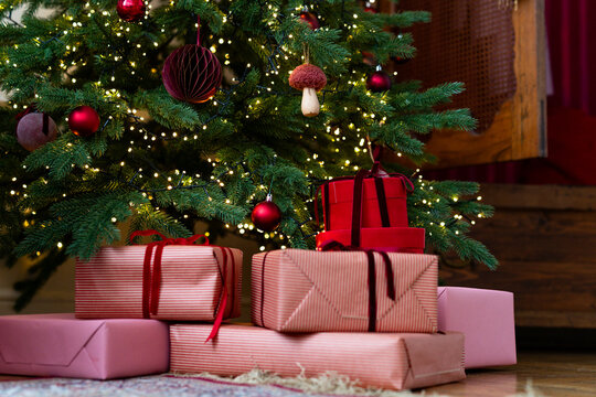 Close-up of a stack of wrapped Christmas gifts under an illuminated Christmas tree in a living room