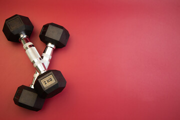 Black dumbbells, each weighing 2 kg, are positioned in a crossed formation on a bright red background, highlighting fitness and strength training essentials