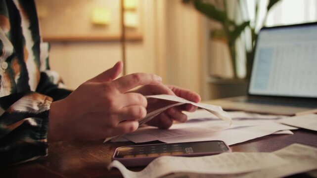 Woman sorts receipts using a calculator to track expenses at home. Budget planning or tax return from home. High quality 4k footage