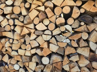 Full frame close-up background of a tightly stacked woodpile with many chopped logs; abstract pattern, natural texture, preparation for heating and winter season, firewood wall.