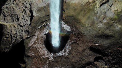 Aerial view of waterfall flowing into rocky gorge in Mulagljufur Canyon. Drone footage revealing a powerful vertical drop framed by dark moss-covered cliffs. - Powered by Adobe