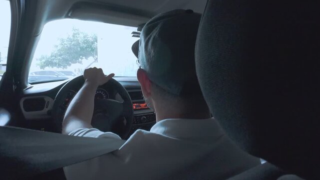 Male driver with a hat and glasses holding the steering wheel and driving a car on a sunny day