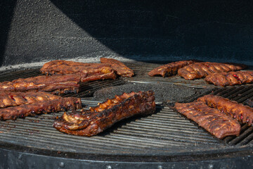 Grilled ribs cooking on round barbecue grill. Delicious barbecue pork ribs with crispy dry rub seasoning placed on circular grill ready for serving.