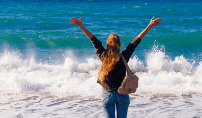 happy woman in casual attire with arms raised up enjoying the sea waving
