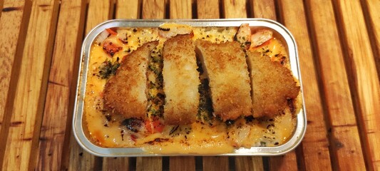 Crispy Chicken Katsu with Japanese Rice Mentai Sauce Served in a Alumunium Foil Container on Wood Table. Culinary Business Concept. Food Photography Presentation