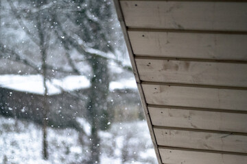 Snowflakes gently fall outside a wooden-roofed building, creating a peaceful winter scene. The...