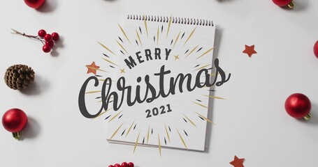 Displaying spiral notepad featuring Merry Christmas 2021 on white tabletop, with baubles, pinecone