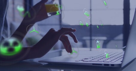 Typing dark-sleeved hands on laptop at home desk, holding glass with orange drink and holograms