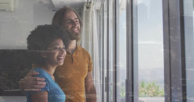Smiling pair hugging, gazing at tall doors with skyline on glass, planters, mustard-tee, blue-top - Powered by Adobe