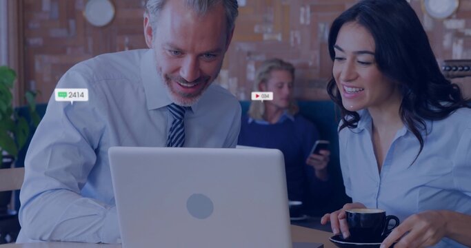 Collaborating business colleagues leaning over laptop at cafe, holding black cup, showing badges