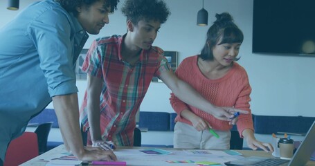 Leaning coworkers wearing coral, plaid and light blue clothing, examining charts and laptop in room