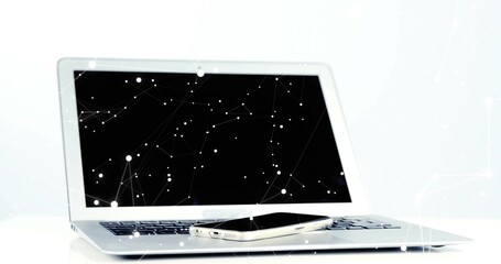 Displaying silver laptop with smartphone resting on keyboard at white desk, showing network overlay